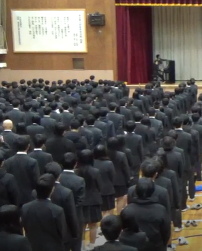 体育館で生徒が立って校歌を斉唱する様子