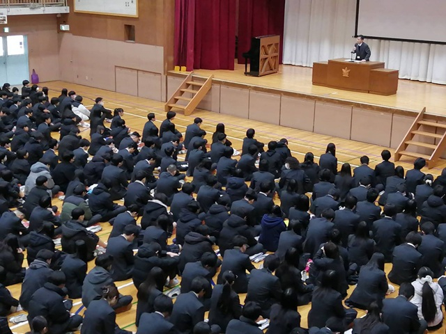 演台で話す校長先生とそれを見つめる生徒